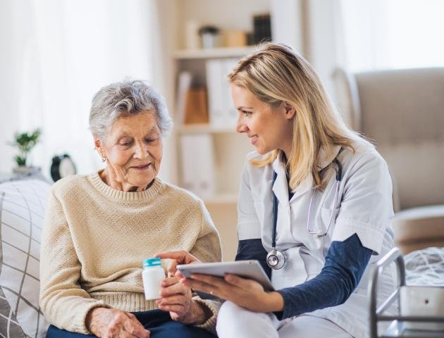 A health visitor with tablet explaining a senior woman how to take pills.